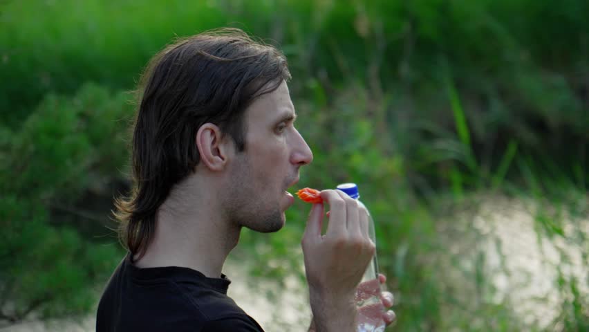 Man enjoys a snack of fruit while holding a bottle of water during a picnic in a grassy meadow
