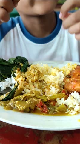 A boy from Indonesia eats balado chicken with gusto. Balado chicken is one of the menus of Padang rice besides rendang. Eating using bare hands without spoons. A unique eating habit in Indonesia