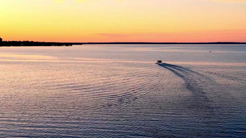 Pontoon boat on a northern Minnesota lake, sailing away from camera at sunset, with intersecting waves. 