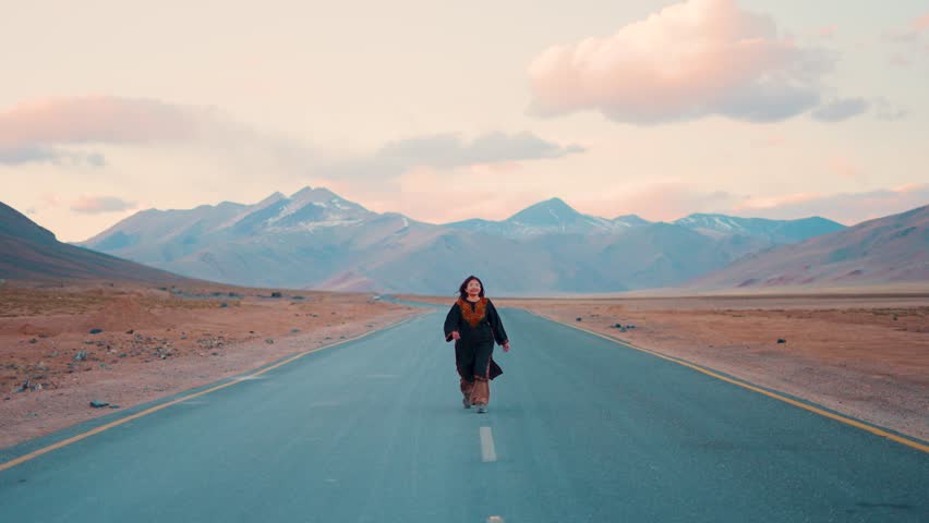 4K shot of Indian travel influencer girl walking on road with mountains in background at More Plains in Ladakh, India. Travel lifestyle. Road trip concept.