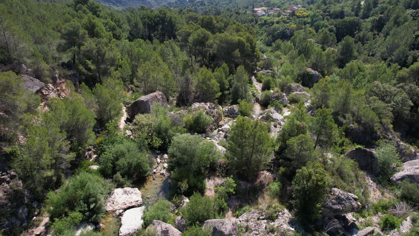 Forward reveal aerial shot of Brugent river valley (popular bouldering area) on sunny summer day. La Riba, Tarragona, Spain.