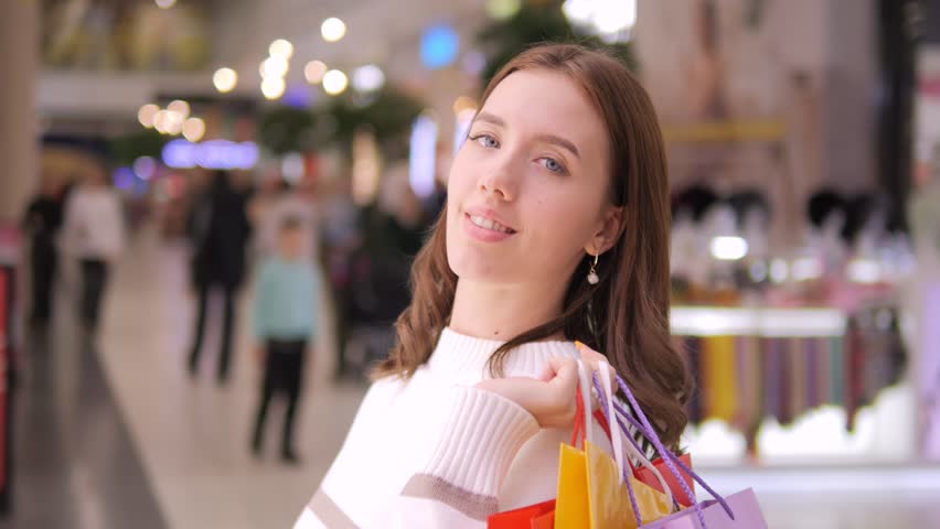 A young woman, filled with joy, proudly displaying her shopping bags in a colorful and vibrant shopping mall