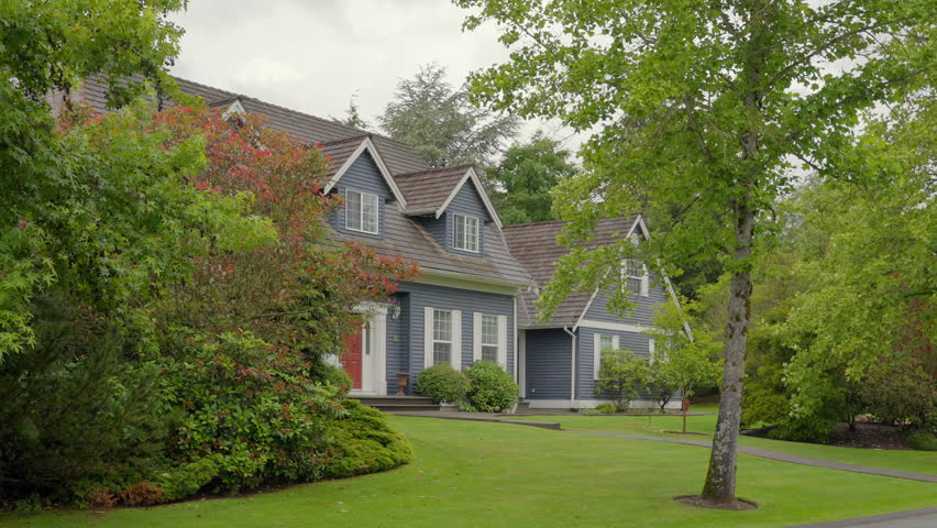 Establishing shot of two story stucco luxury house with big tree and nice landscape at spring rainfall in Vancouver, Canada, North America. Day time on June 2024. ProRes 422 HQ.