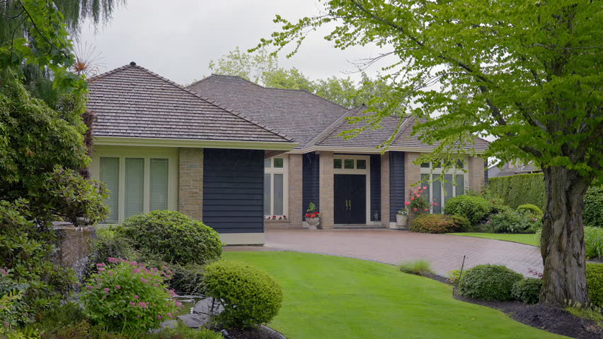 Establishing shot of two story stucco luxury house with big tree and nice landscape at spring rainfall in Vancouver, Canada, North America. Day time on June 2024. ProRes 422 HQ.