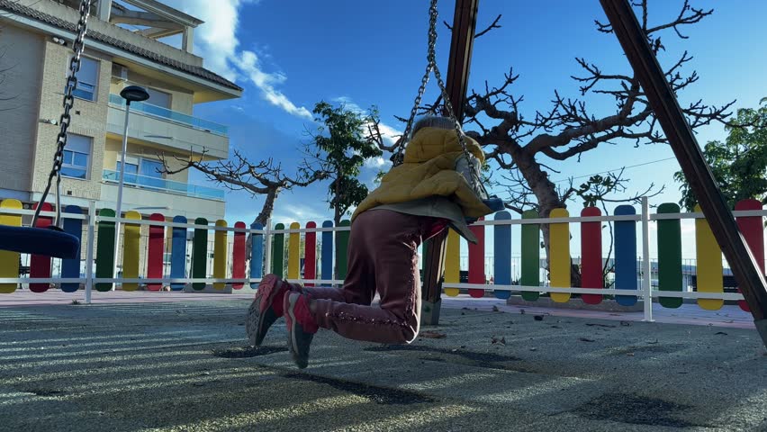 Caucasian child ride on swing in park. Cute girl wearing yellow hooded vest spinning on net swing in parkground. Slow motion