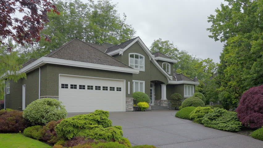 Establishing shot of two story stucco luxury house with big tree and nice landscape at spring rainfall in Vancouver, Canada, North America. Day time on June 2024. ProRes 422 HQ.
