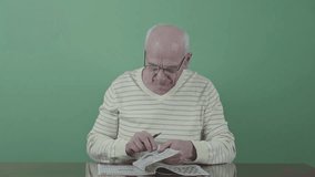 Elderly man wearing glasses solving crossword puzzle with pen while sitting at table. His focused expression shows deep concentration against green background with chromakey - Powered by Shutterstock - Get 15% off with code: PIKWIZARD15