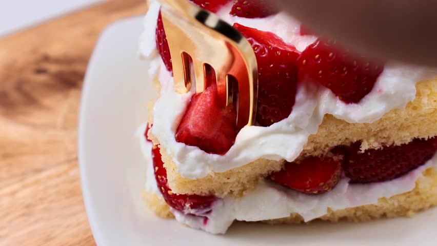 Eating strawberry shortcake with fresh strawberries and whipped cream with a fork close up