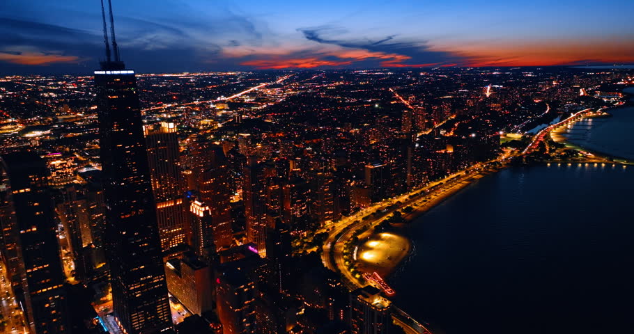 Beautiful scenery of Chicago, IL, United States at night. Multiple cars move by the luminous Lakeshore Drive. Amazing orange sky above the cityscape at backdrop.