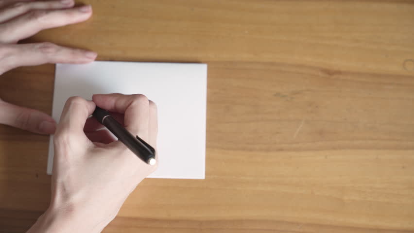 Hands writing the word “2025” in black ink on white paper atop a wooden desk, symbolizing plans, goals, and aspirations for the upcoming year