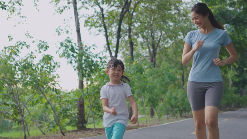 Asian young mother and daughter doing running exercise in the garden. Happy family, attractive mommy in sportswear feeling happy and relax practice workout in public park with adorable girl for health