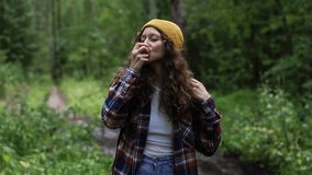 Woman with backpack talks holding apple walking in forest with dense trees. Relaxed young female in knitted hat eats juicy fruit enjoying sweet taste and stunning wild nature during hiking on weekend - Powered by Shutterstock - Get 15% off with code: PIKWIZARD15
