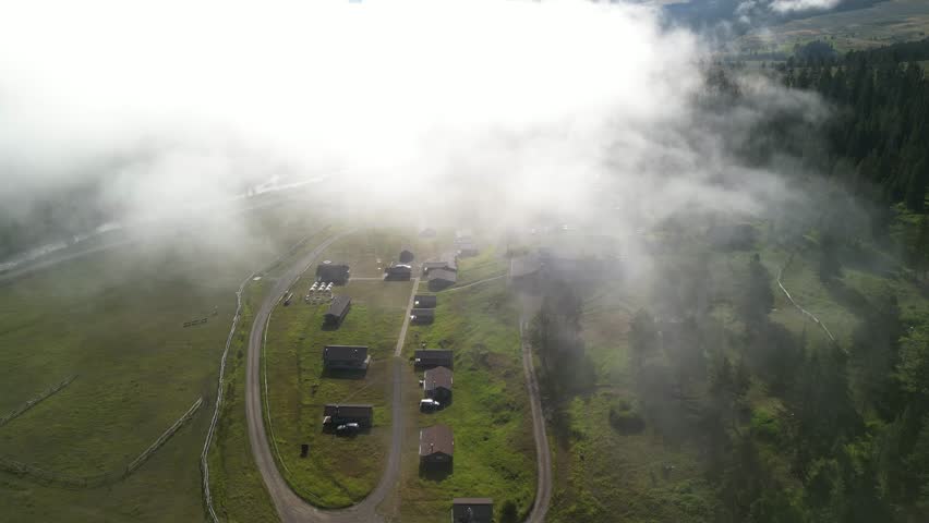 Aerial above mountain cabins in Montana below low clouds in Madison Range in summer