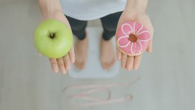 woman on weight scale and hand hold green Apple and donut, choose between fruit is Healthy and sweet is Unhealthy junk food. Dieting control, Weight loss, Obesity, eating lifestyle and nutrition - Powered by Shutterstock - Get 15% off with code: PIKWIZARD15