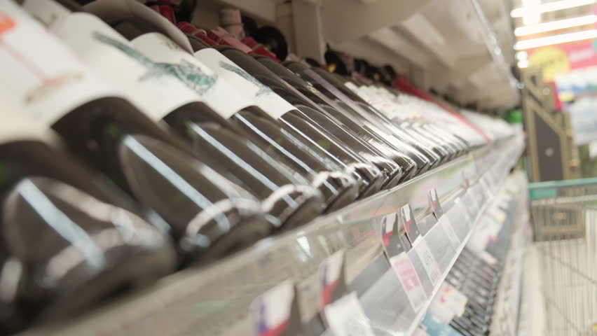 Buyer reads label on bottle of wine on counter when choosing before purchasing.