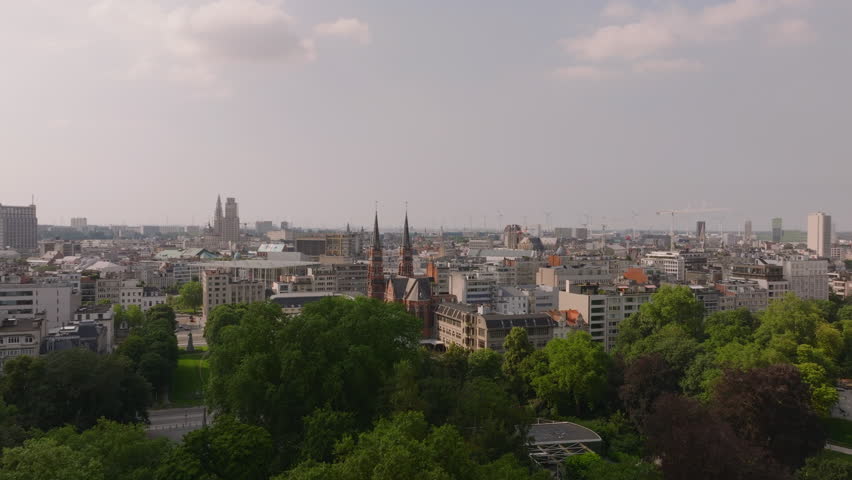 Skyline of Antwerp, Belgium, unfolds under a partly cloudy sky. Lush green trees enrich the urban scenery, harmonizing nature with city life
