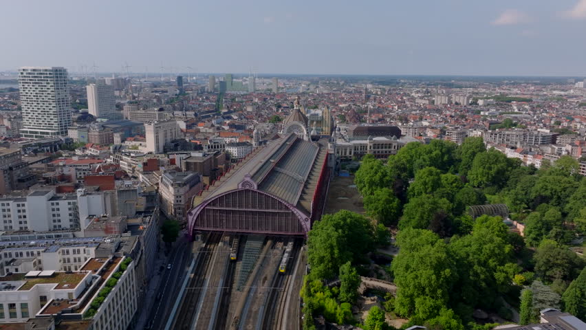 Antwerp Central Station with its recognizable arched roof captured from a high vantage point. Cars are driving on the streets below and trains are arriving at the platforms