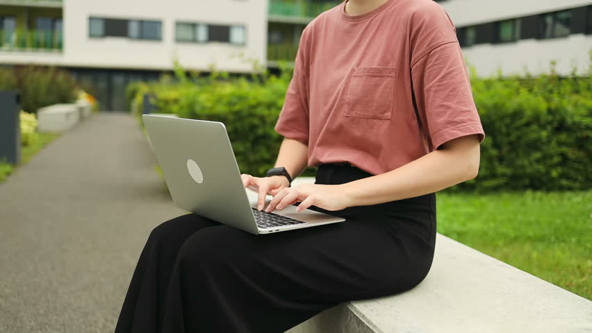 Caucasian woman in at-shirt working on a laptop at city centre Female student on campus sitting on a bench. High quality FullHD footage