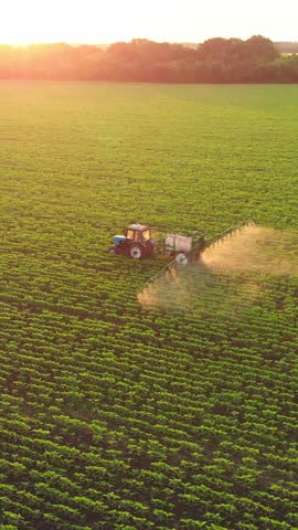 Modern irrigation system in farm fields, farmer on tractor watering agricultural field in summer, aerial view, vertical video. Picturesque landscape with farmland, slow motion, grow organic cereals