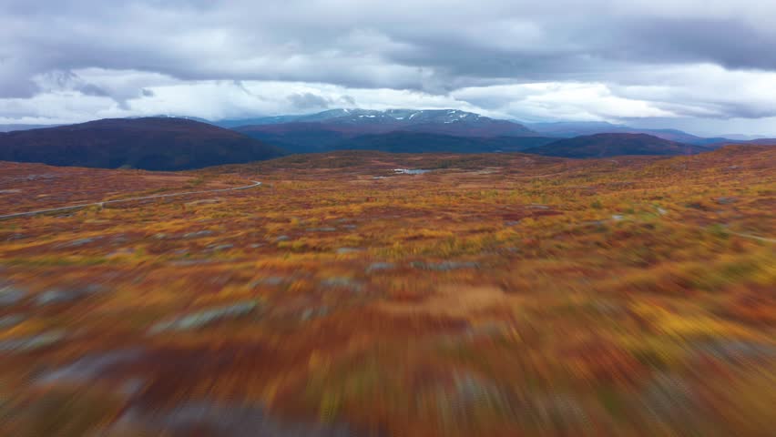 Fast forward aerial shot of the colorful autumn tundra landscape.Heavy clouds in the sky. Mountains tower on the horizon.