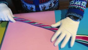 A person making Christmas sugar sticks cutting a ribbon with scissors on a pink table. The ribbon is striped and has a Christmas theme - Powered by Shutterstock - Get 15% off with code: PIKWIZARD15