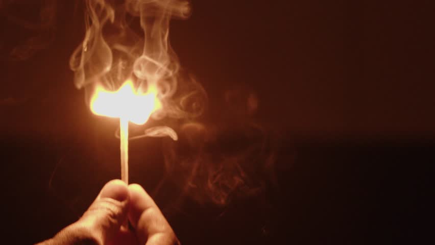 Photography for dynamic scenes, ignition, a flame flickering on a matchstick with smoke rising as it burns on a dark background