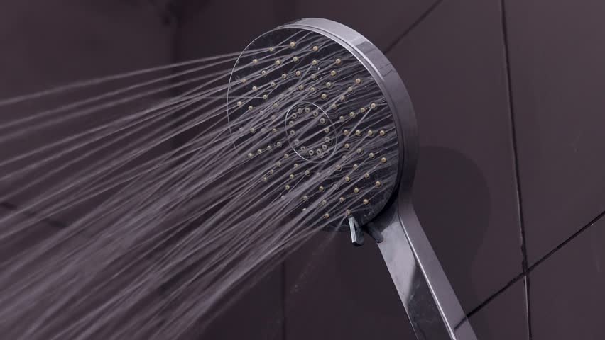 Photography for dynamic scenes, water, shower head opening, and water starts pouring from it in a bathroom with dark gray tiles