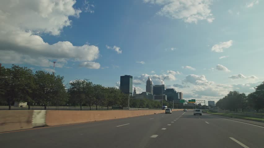 Car Point of View POV moving towards Ohio city of Cleveland, OH on Lake Erie movement out window with Midwest cityscape, towers, offices, buildings, and vehicle traffic on multi-lane highway road
