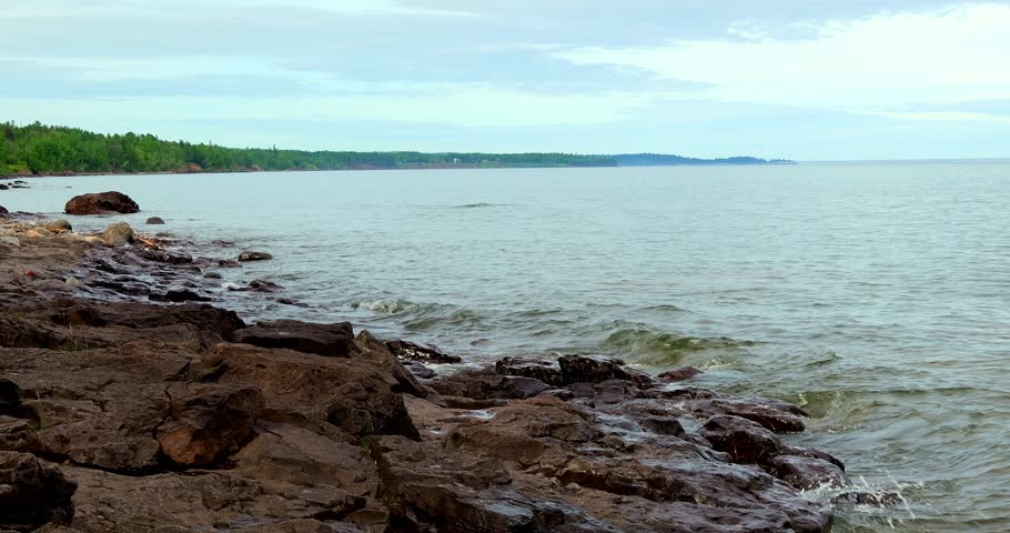 Dramatic rocky shoreline of the North Shore of Lake Superior on a cloudy day, with splashing water wetting the rocks. Zoom out.