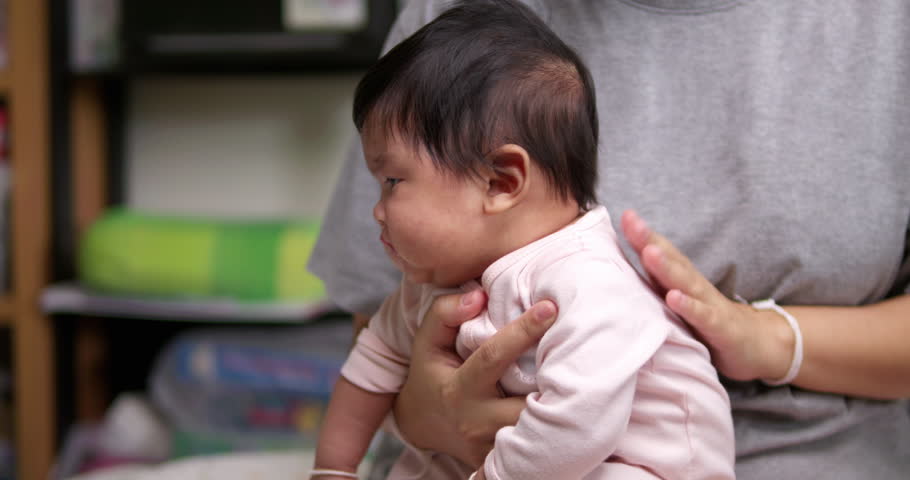 Holding up a newborn child's neck as the mother is tapping the baby's back to help her burp and belch out some gas after having some milk.