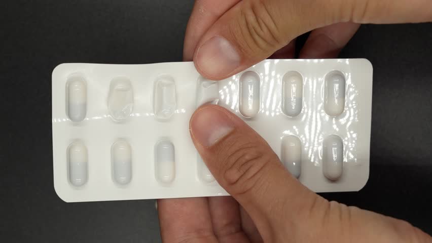 A close-up image shows hands carefully pressing a single capsule out of a blister pack. The fingers gently push the capsule through the foil, emphasizing the precision and care involved in the process