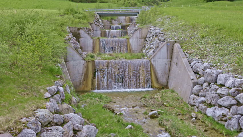 Water falls from man made cascade. Water flows around the stones in the river. Traeschlibach near Beckenried, Canton Nidwalden, Switzerland.