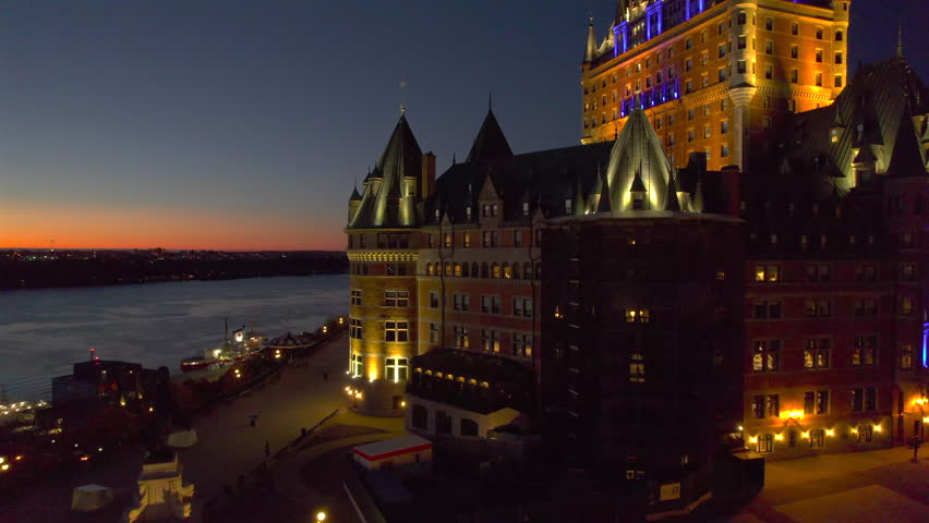 Aerial view of Quebec City at sunset with the Canadian flag waving above historic architecture. Warm golden light over Old Quebec with Château Frontenac in the background. Perfect for travel, tourism, culture, heritage, and national identity concepts.