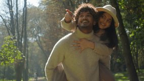 Carefree loving Indian Arabic couple smiling man boyfriend boy carry holding woman girl girlfriend piggyback male female hug talking in park outdoors strolling pointing look at nature date closeness - Powered by Shutterstock - Get 15% off with code: PIKWIZARD15