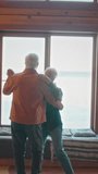 Full vertical shot of romantic elderly Caucasian husband and wife slow-dancing together in living room at country home, in front of window, swaying to rhythm of retro music and chatting - Powered by Shutterstock - Get 15% off with code: PIKWIZARD15