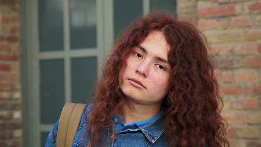 Individual close up portrait of a serious student standing and looking at camera at university campus. Thoughtful teenager holding a notebook at highschool. Young adult person staring front at academy