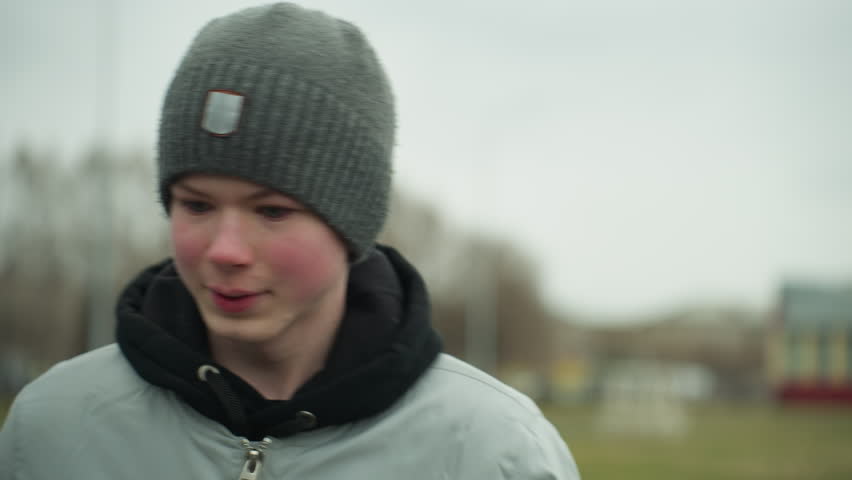 Close-up of a young boy jogging on a track in a stadium, appearing focused from, the background is blurred, showing a football field