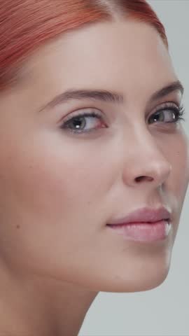 Vertical studio portrait of young, beautiful and natural redhead woman applying skin care cream. Face lifting, cosmetics and make-up concept.
