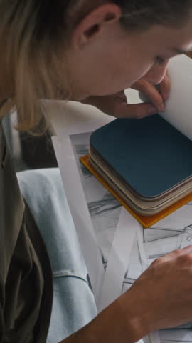 Vertical shot of seamster selecting garments and colors for new collection of clothes at table