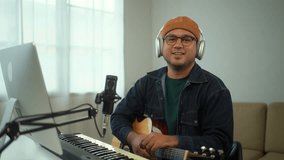 Happy Young asian musician playing guitar and confidently smiling to camera sitting at digital recording home studio room, a composer man mastering music audio for soundtrack with piano keyboard.
 - Powered by Shutterstock - Get 15% off with code: PIKWIZARD15