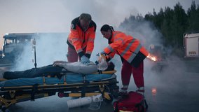 Ambulance Paramedics in High Visibility Uniform Administer Critical Care to an Injured Male on a Stretcher. Smoke and Emergency Vehicles Surround a Serious Road Accident or Disaster - Powered by Shutterstock - Get 15% off with code: PIKWIZARD15