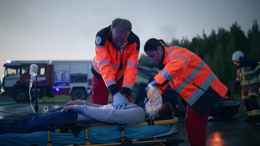 Female and Male Paramedic Rescue Team Saving Life of a Young Male Involved in a Traffic Accident. Doctors Performing Emergency CPR, Compressing His Chest and Providing Artificial Ventilation