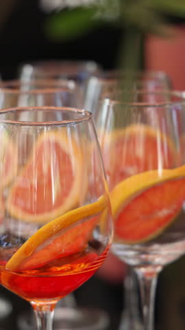 cocktail bar for events in restaurant.many glasses in row with beverage, slice of orange,lime and grapefruit inside.aperol spritz or other alcoholic cocktail.video through olive tree leaves.