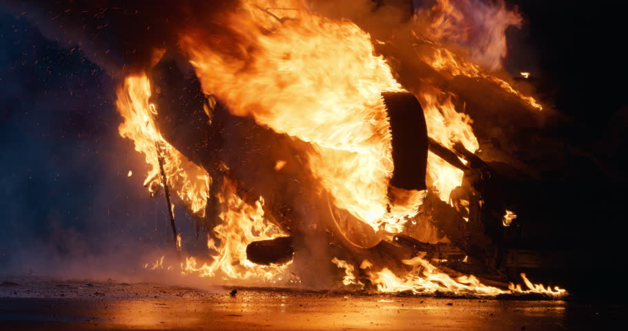 Car Accident with an Overturned Vehicle Engulfed in Flames After the Crash on a Motorway at Night. Bright Intense Fire on a Wet Highway Road. Close Up Footage Without People