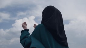 Muslim Woman in a Fluttering Dress Praying to God with Hands Raised Outdoors Under the Clouds. Concept of Islam, faith, spirituality, hope, worship, dua, belief, religion, prayer - Powered by Shutterstock - Get 15% off with code: PIKWIZARD15