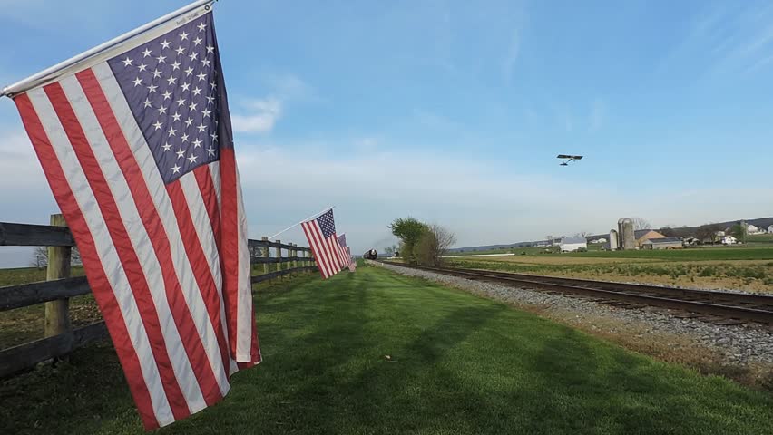 American Flags Line the Railway Near a Farm on a Clear Day