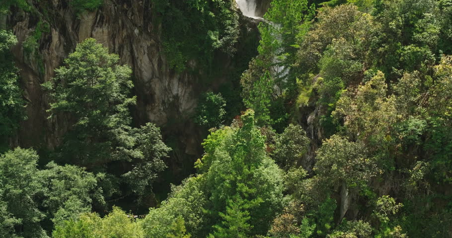 Aerial view from the hillside captures a mesmerizing waterfall cascading through a wild, dense forest in Nepal. The lush greenery enhances the natural beauty and serene atmosphere of the scene.
