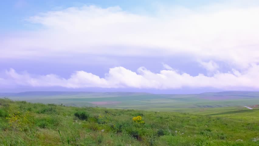 A strong wind carries clouds quickly over a green meadow. The wind sways the grass. Clouds against the blue sky close-up. Weather changes during the rainy season. Storm clouds.