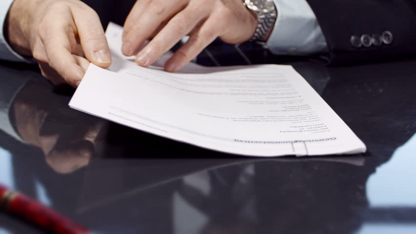 Businessman sitting at shiny office desk signing a contract with noble pen