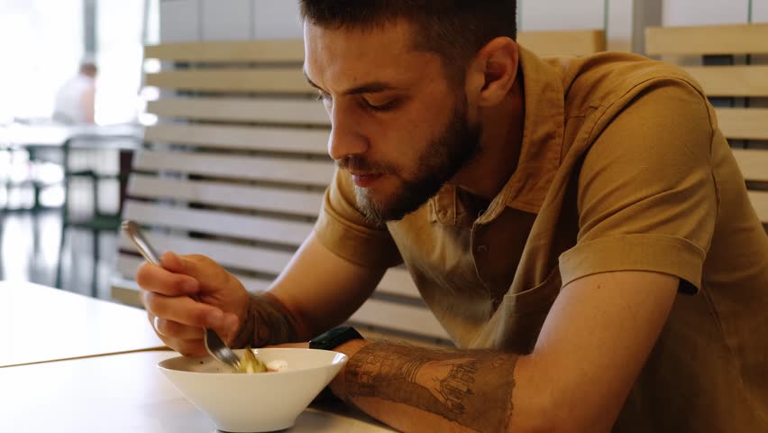 Dinner and meal with organic products concept. Young man eating delicious fresh Greek salad with vegetables, cheese and olive oil in cafe. Vegetarian cuisine and healthy vegetable diet